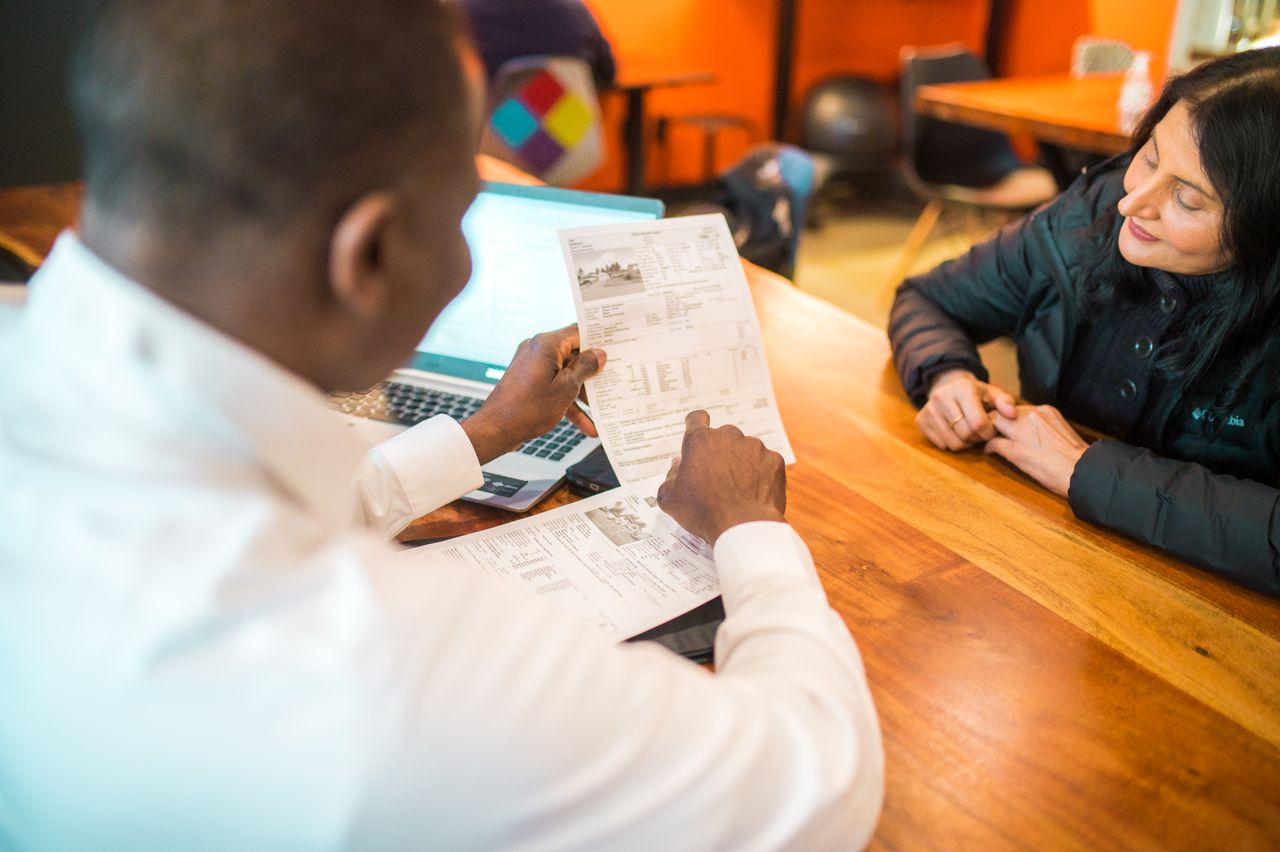 Two adults discussing documents in a bookkeeping setting indoors.